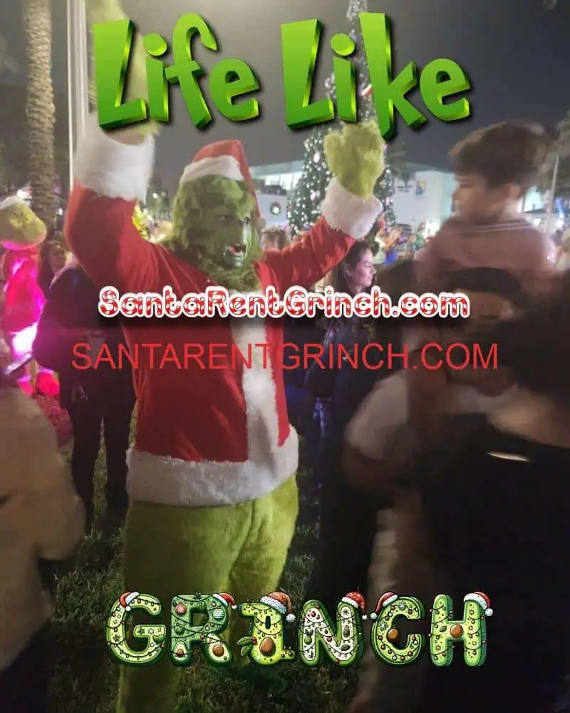 Grinch in a Santa coat waving his arms at a crowded outdoor holiday event at night
